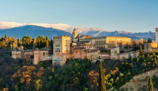 Classical Spain Alhambra palace in Granada with snow-capped Sierra Nevada mountains in background and surrounding cypress trees
